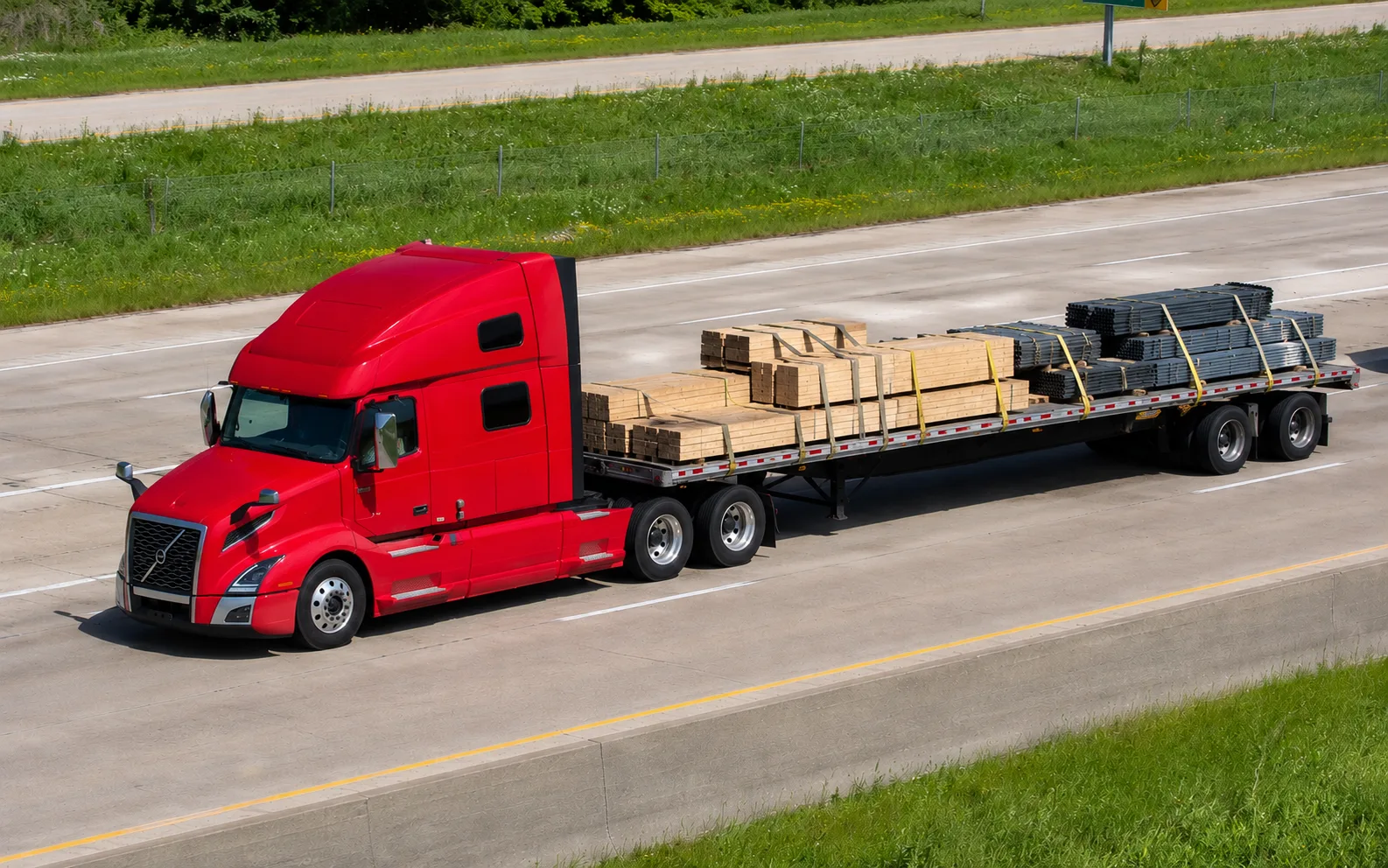 Flatbed trailer loaded with secured lumber and steel on the highway